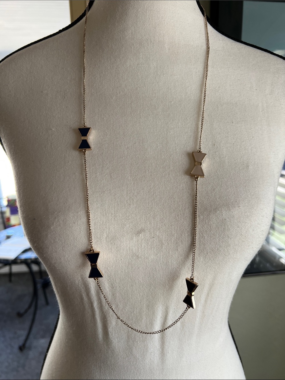 Gold tone necklace with blue and white reversible enamel bows. 34” long